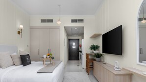 A modern hotel room with a bed, bedside table, TV, and a view into the kitchen area. - Maison Privee - Stylish Studio w/ Top Facilities in Damac Hills (Dubai)