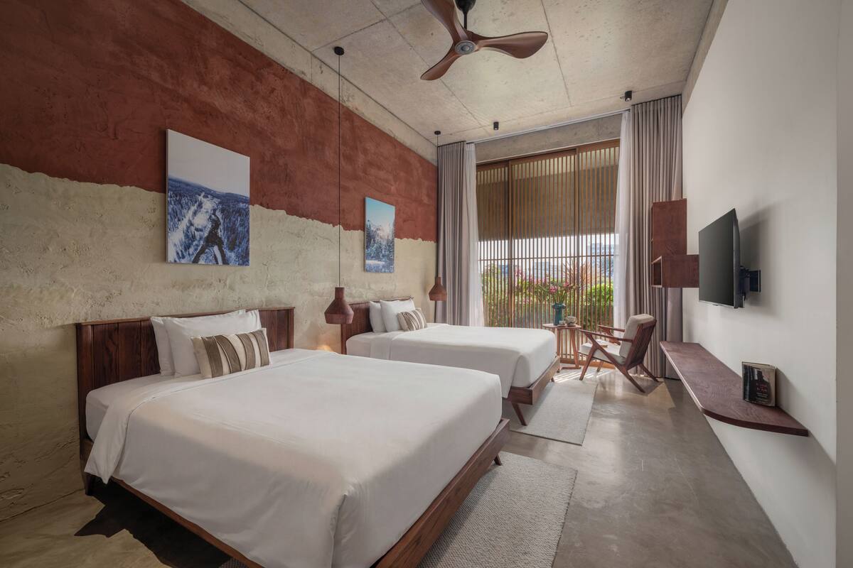 Une chambre d’hôtel avec deux lits, un ventilateur de plafond, une télévision et un balcon avec vue.