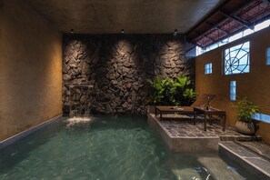 A spa area with a stone wall, a small waterfall, and a seating area with a potted plant.