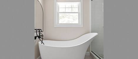 A modern bathroom with a freestanding bathtub, a window, and a shower area.