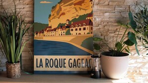 Ein gerahmtes Kunstwerk, das eine Küstenstadt mit einer Klippe zeigt, beschriftet mit 'LA ROQUE GAGEAC'.