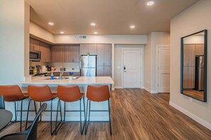 A modern kitchen with wooden cabinets, a central island with bar stools, and a refrigerator. - Tempe DT Escape | Pool, Gym, W/D, Parking Sleeps 4 (Tempe)