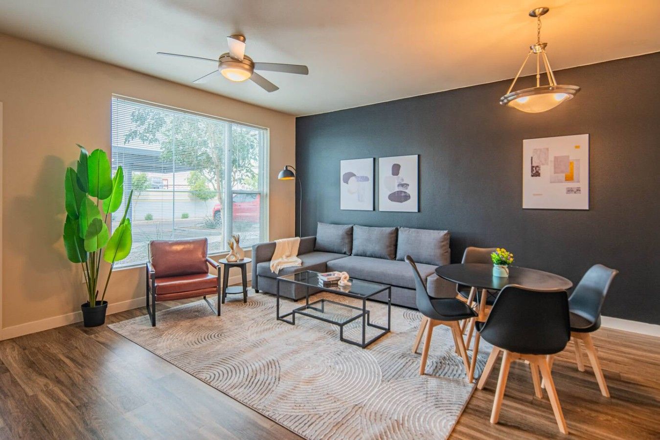 A modern living room with a sofa, coffee table, and chairs, a dining table with chairs, a ceiling fan, and artwork on the walls.