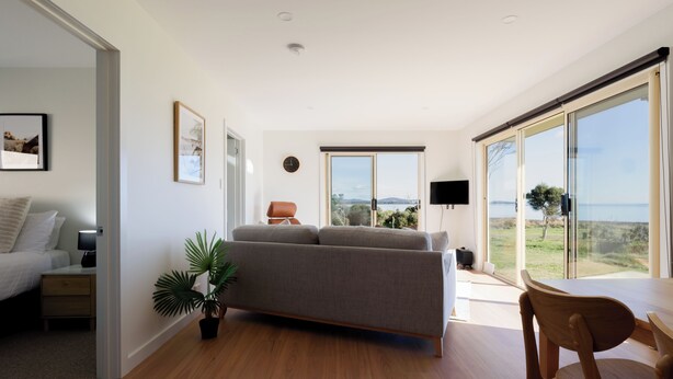 A modern living room with a sofa, a dining table, and a large window offering a view of the outdoors.