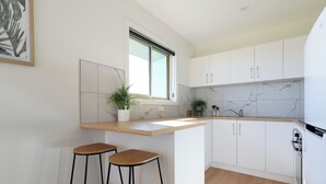 A modern kitchen with white cabinets, a marble backsplash, and two wooden stools.