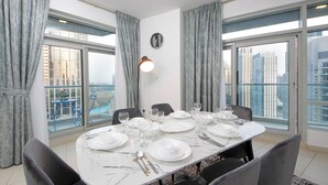 Un comedor con una mesa redonda dispuesta para seis personas, ventanas amplias con cortinas y vistas a la ciudad.