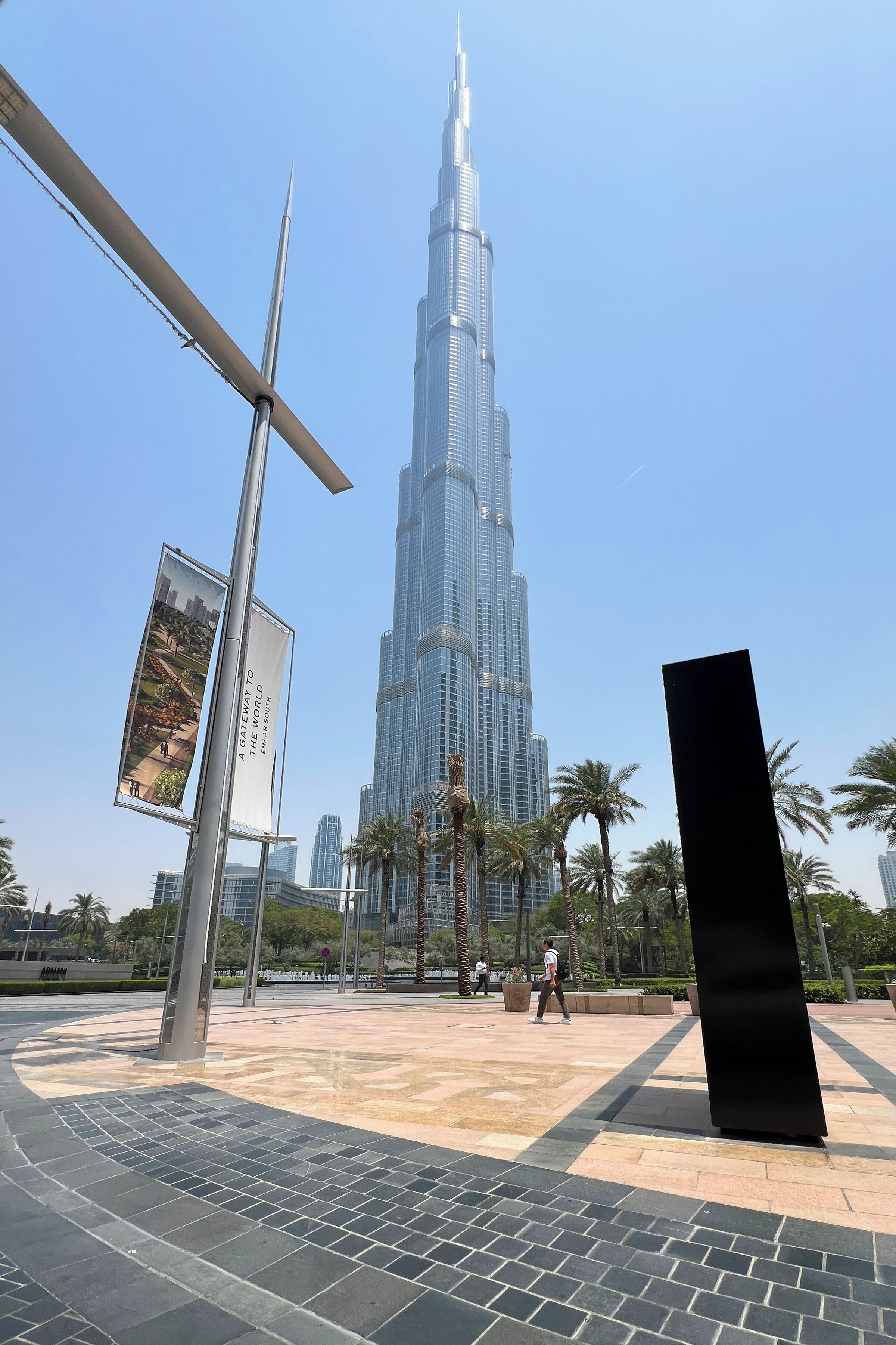 Uitzicht op de Burj Khalifa, met een modern plein voorop, inclusief een groot zwart beeld en een spandoek.