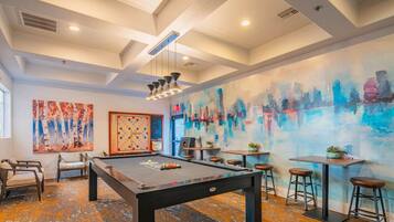 A billiards room with a pool table, chairs, and a colorful abstract mural on the wall.