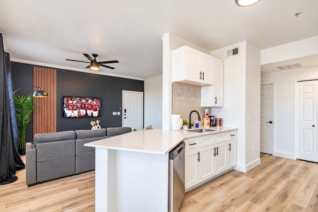 A modern kitchen with white cabinetry, a built-in dishwasher, and a gray sofa in the living area.