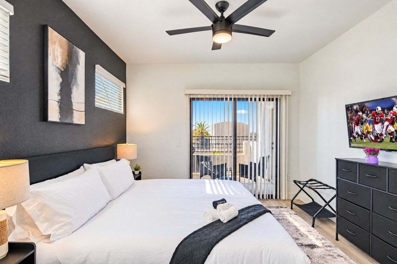 A modern hotel room with a bed, a ceiling fan, a TV, and a balcony with a view.