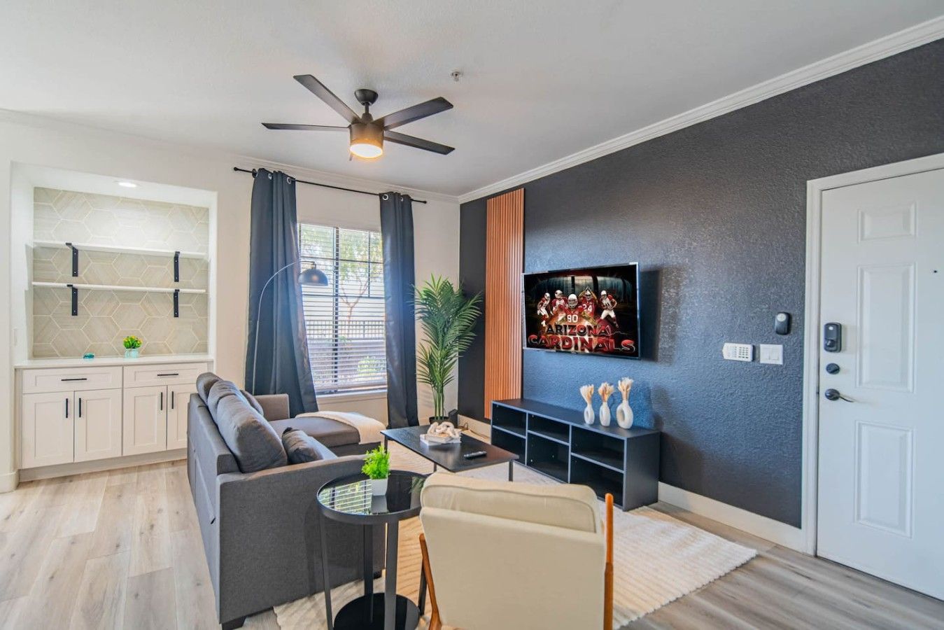 Een moderne woonkamer met een bank, een salontafel, een aan de muur bevestigde televisie en een plafondventilator.