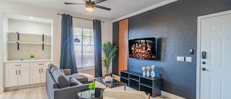 Een moderne woonkamer met een bank, een salontafel, een aan de muur bevestigde televisie en een plafondventilator.