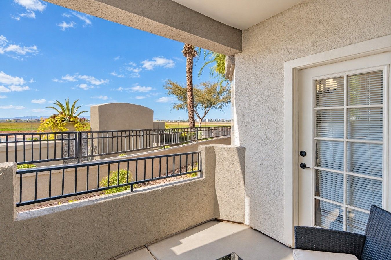 A balcony with a view of a palm tree and a distant landscape, a door with a window, and a small seating area.