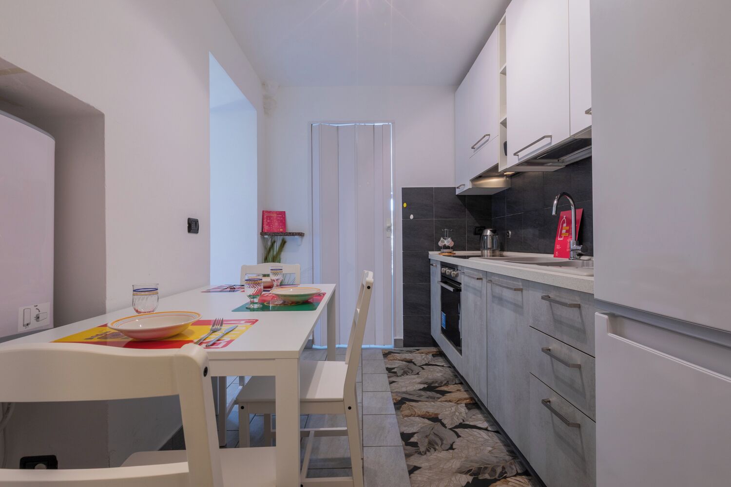 Une cuisine étroite avec un coin repas. On y trouve une table avec des chaises, un évier et des placards.