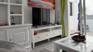 Un salon moderne doté d’un téléviseur à écran plat, de meubles blancs, d’une table basse en verre et d’un tableau placé au-dessus du téléviseur.