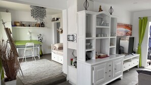 Un salon moderne avec un meuble de rangement blanc pour la télévision, un canapé vert et un coin repas avec une table et des chaises vertes.