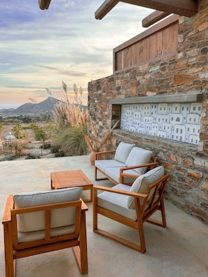 A stone wall with a built-in fireplace and outdoor seating area with wooden furniture. - Elysian Villas Ios (Ios)