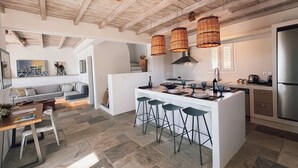 Cocina moderna con una isla central, taburetes de bar y una zona de comedor con sofá y mesa.