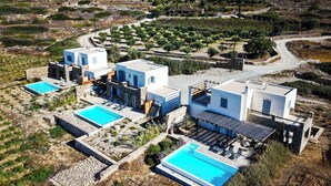 Una villa moderna con varias piscinas, rodeada de jardines en terrazas y un paisaje montañoso.