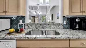 Una cocina con encimera de granito, pileta de acero inoxidable y armarios de madera.