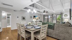 Un comedor con una mesa de madera dispuesta para cuatro personas, rodeada de sillas. Un candelabro cuelga del techo, y se observa un ventilador de techo.