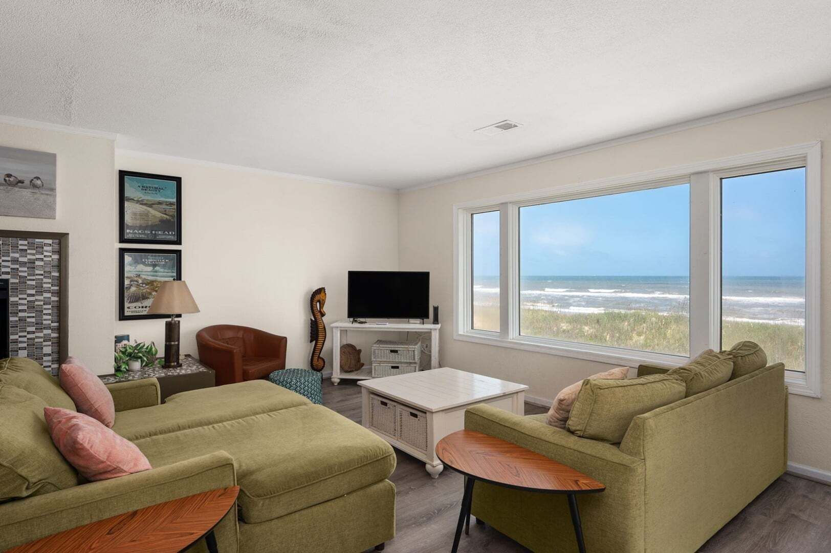 A living room with a large window overlooking the beach, a television, and a cozy seating area.
