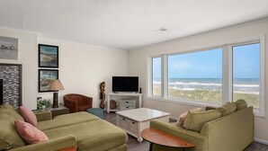 A living room with a large window overlooking the beach, a television, and a cozy seating area.