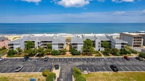 A multi-story hotel with a parking lot in front, overlooking a beach and ocean.
