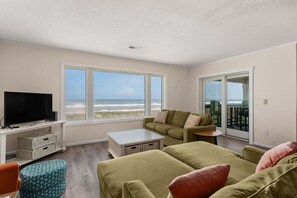 Un salon avec un téléviseur, un canapé, une table basse et une vue sur la plage.
