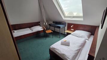 Una habitación de hotel pequeña y funcional con dos camas individuales, un escritorio y una silla.