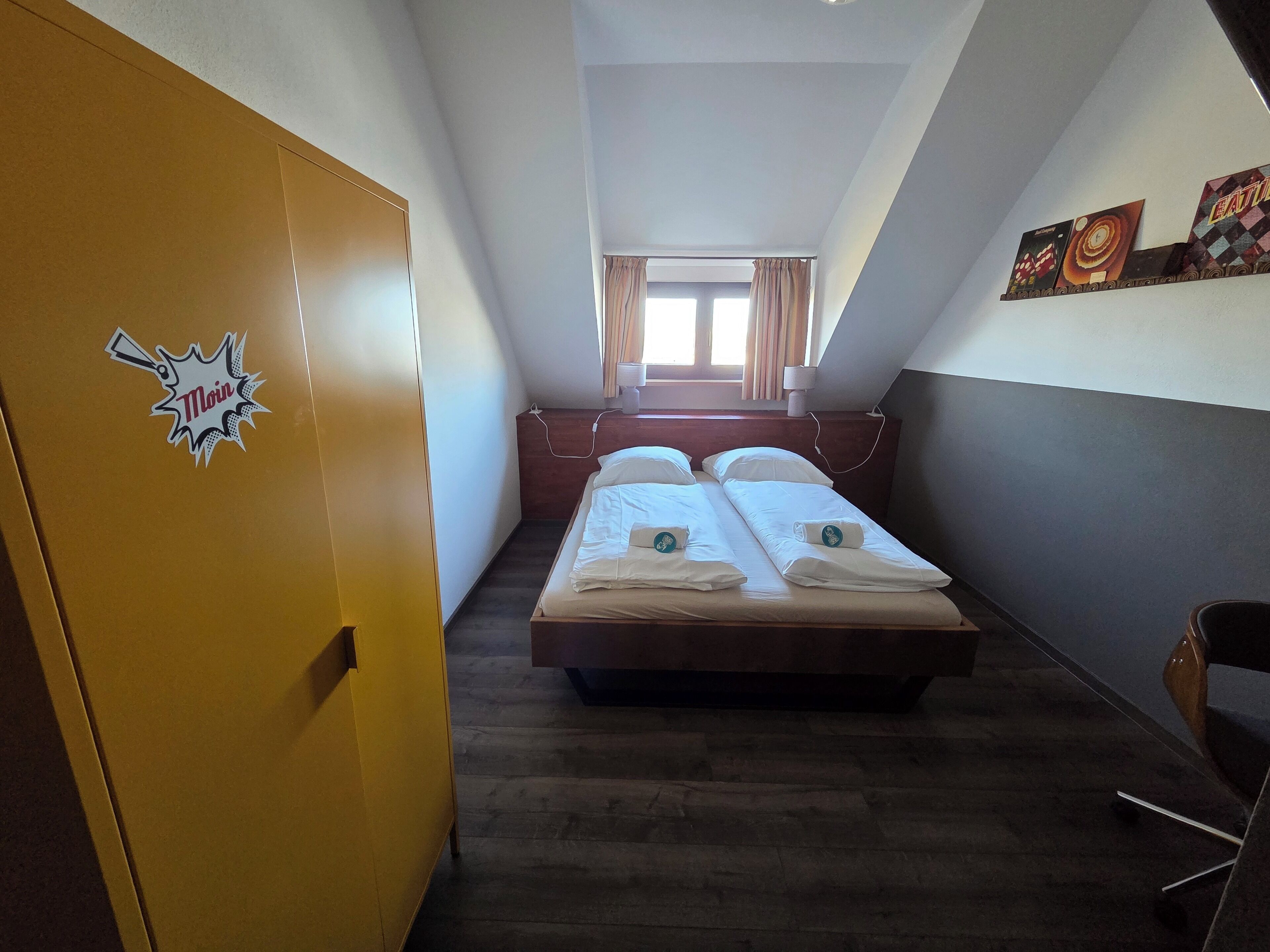 A narrow room with a bed, a yellow wardrobe, and a window with curtains.