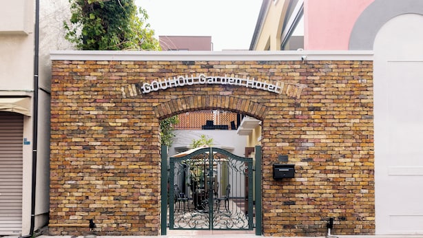 A brick wall with a gate and a sign that reads 'GOUHOU Garden Hotel.' - Gouhou Garden Hotel (Tokyo)