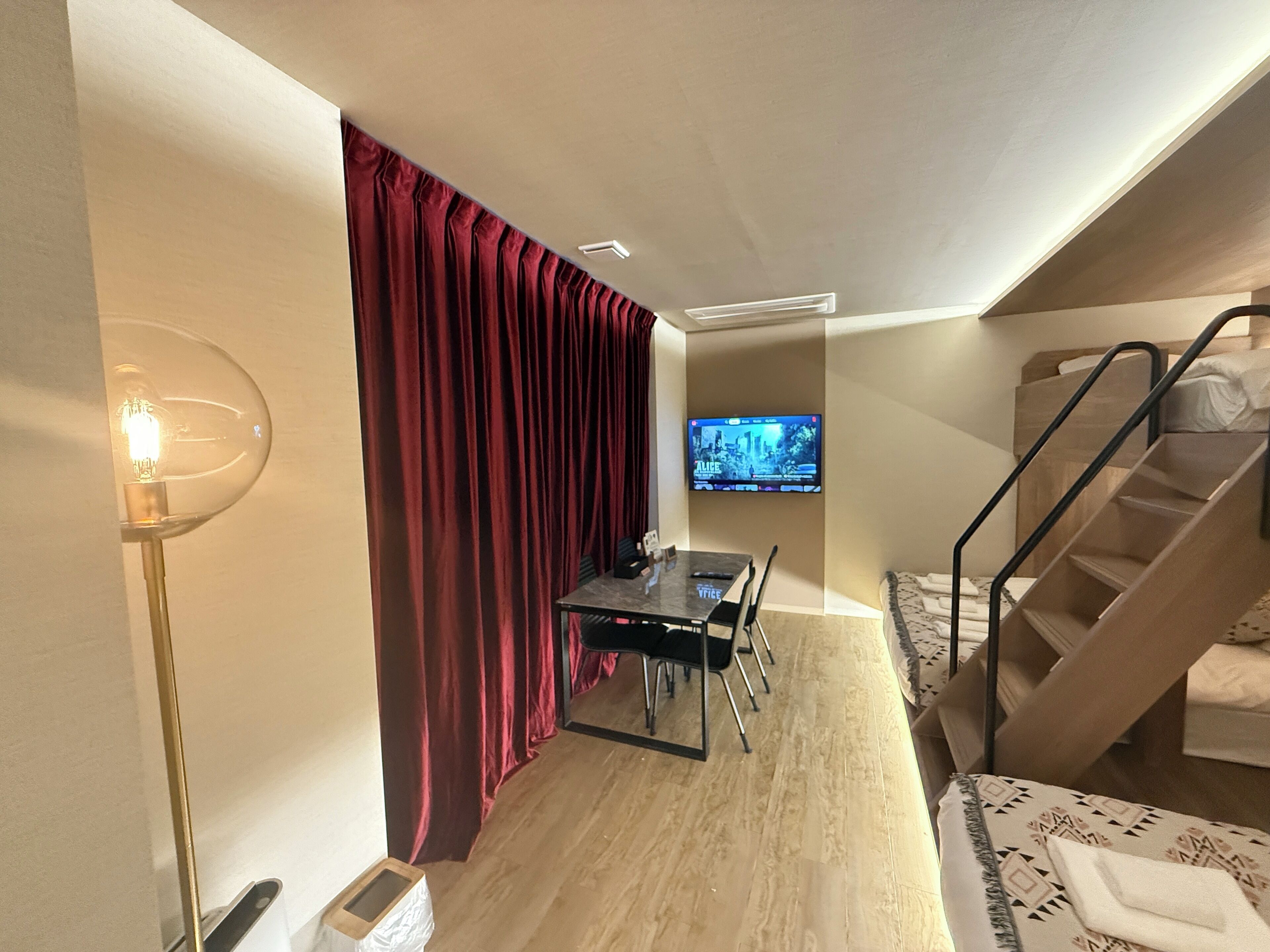 Habitación de hotel compacta con zona de comedor, televisor montado en la pared y una escalera.