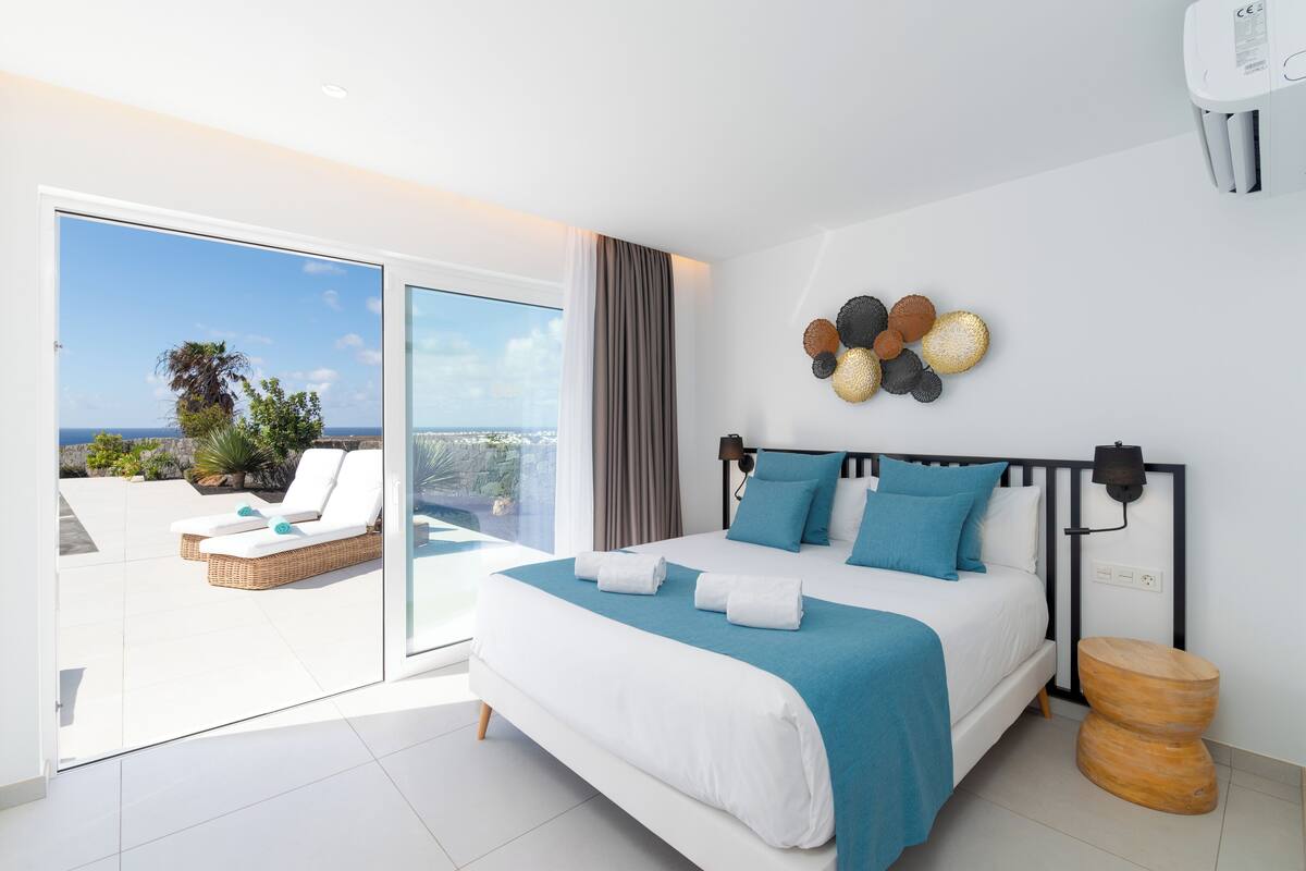 Une chambre avec un grand lit, une vue sur l’extérieur et un ventilateur de plafond.