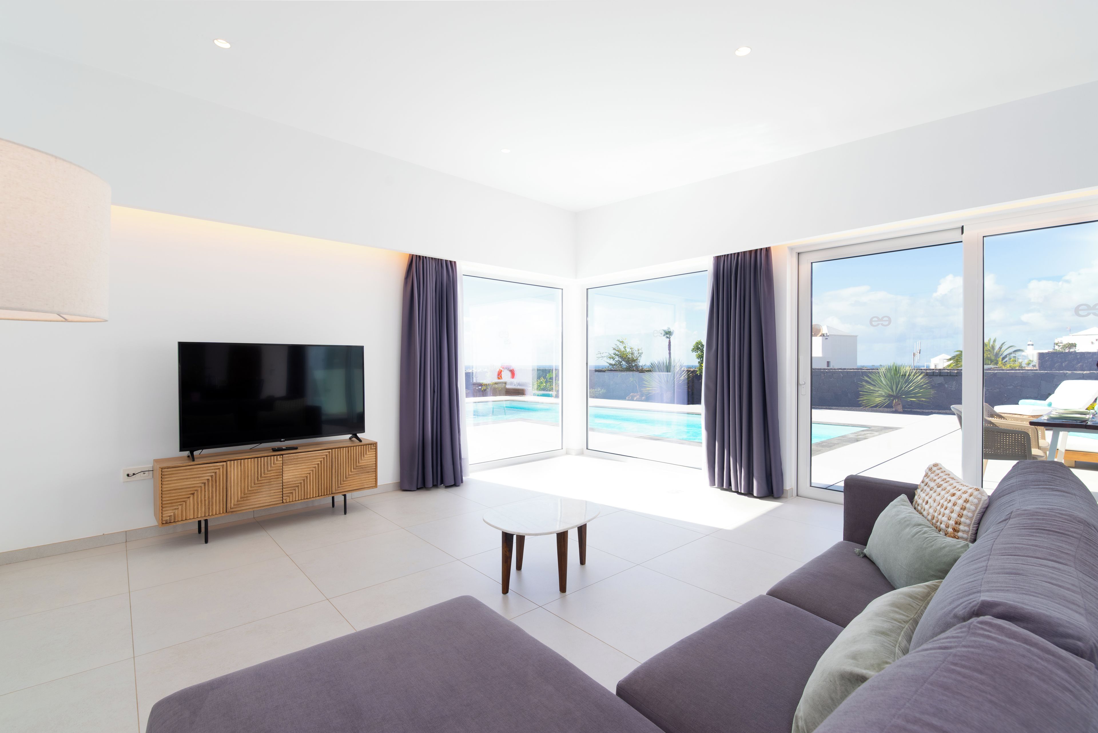 A modern living room with a flat-screen TV, a white coffee table, and a grey sofa.