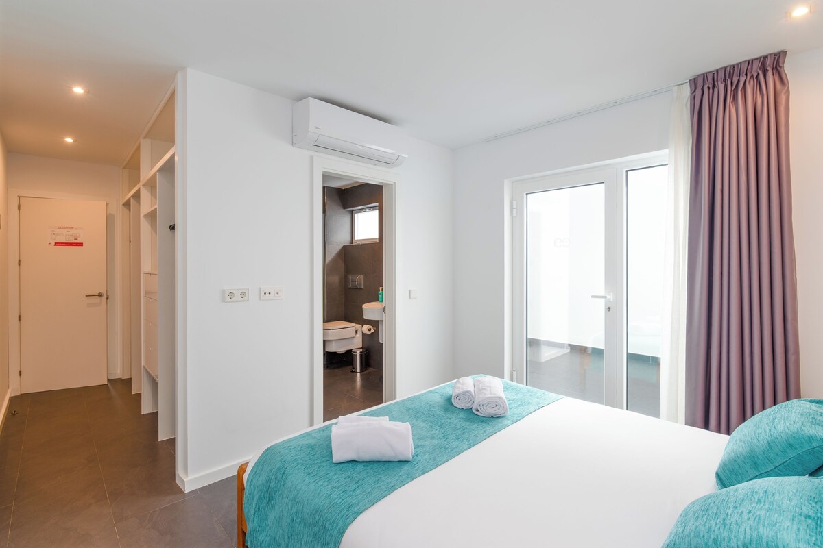 A hotel room with a bed, a bathroom, and a sliding door to a balcony.