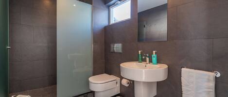 Ein modernes Badezimmer mit einer Duschkabine aus Glas, einer weißen Toilette, einem Waschbecken mit Spiegel darüber und einem Handtuch an einem Halter.