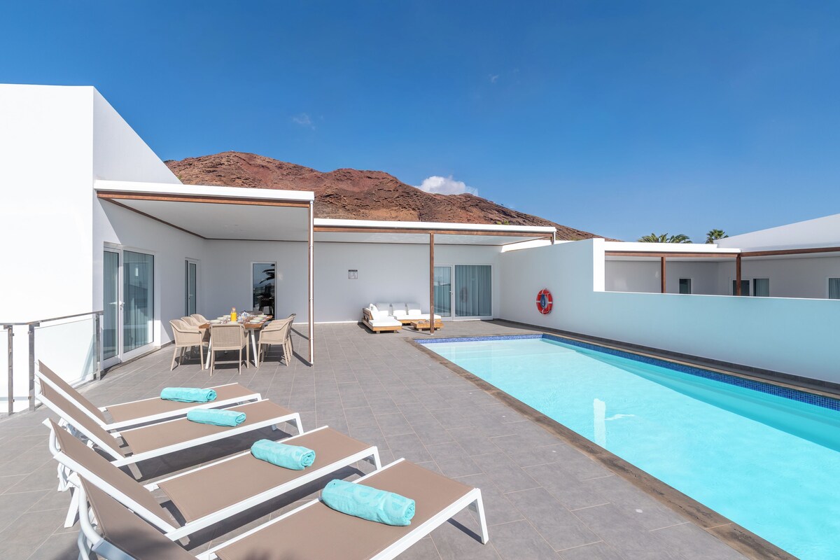 Un hotel moderno con piscina, tumbonas y comedor.