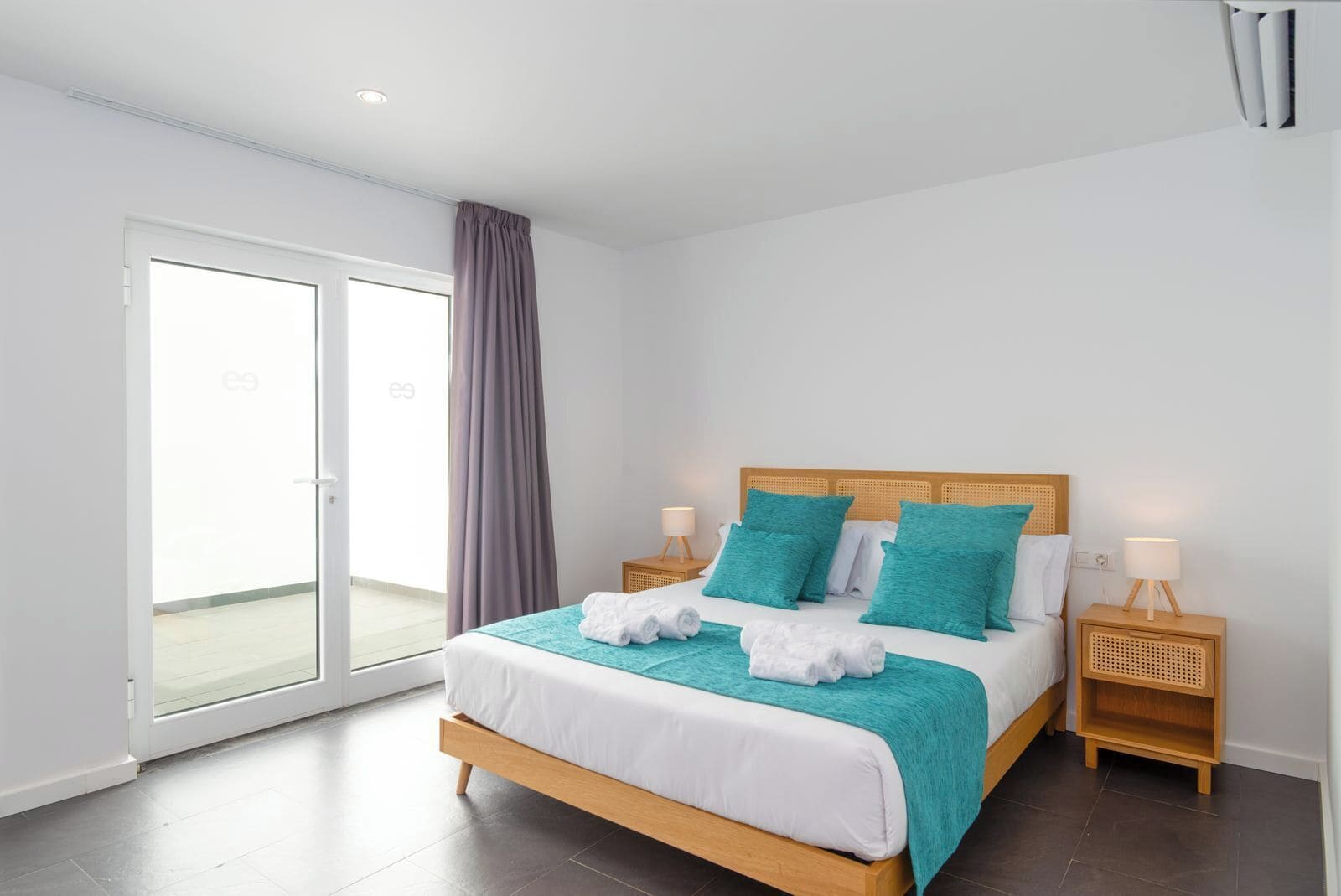 Habitación de hotel moderna con una cama grande, dos mesitas de noche, una puerta corrediza de vidrio y vistas al exterior.