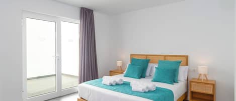 Habitación de hotel moderna con una cama grande, dos mesitas de noche, una puerta corrediza de vidrio y vistas al exterior.