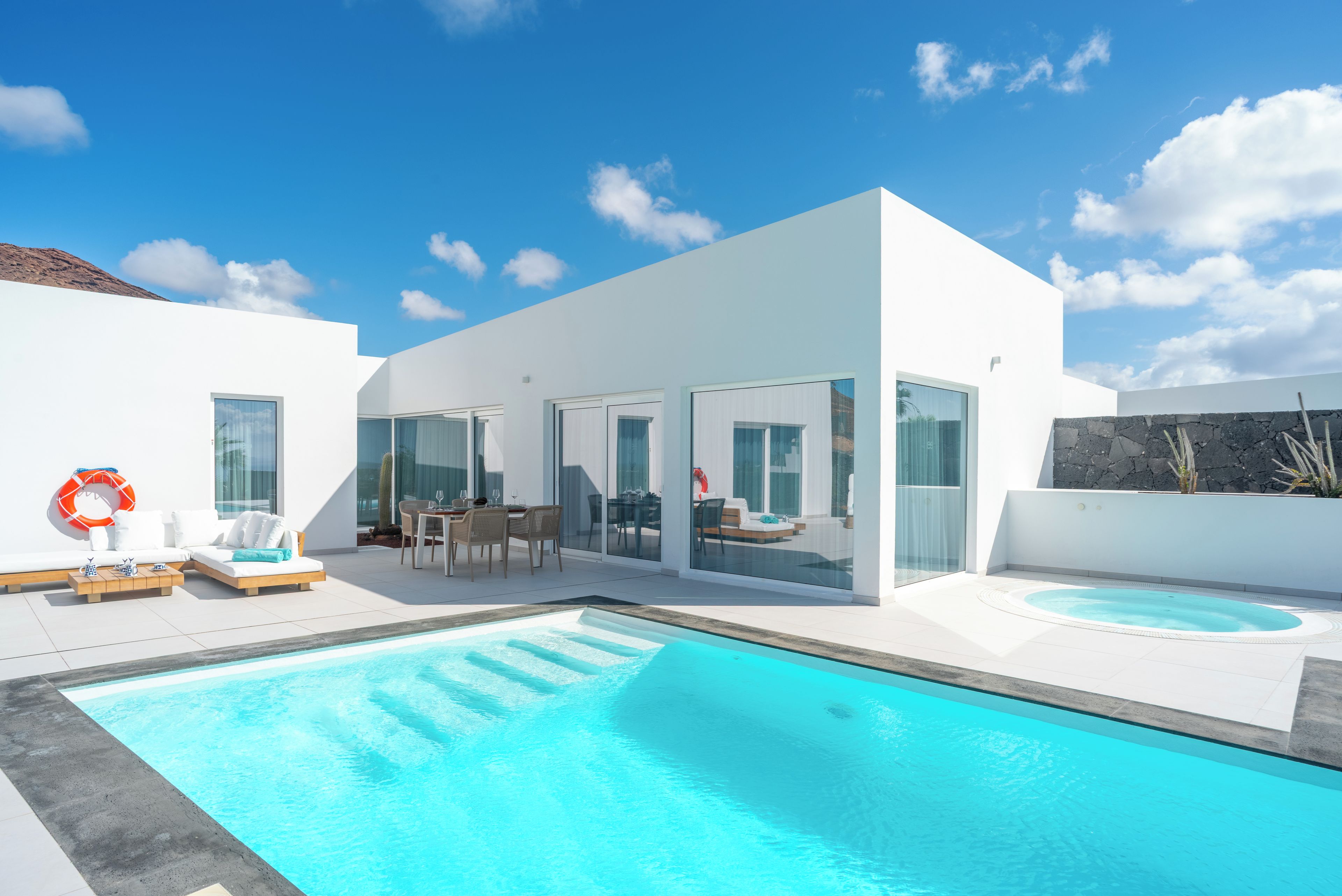 Un espace piscine moderne doté d’une piscine à l’eau cristalline, d’un jacuzzi et d’un coin salon avec un canapé et des fauteuils.