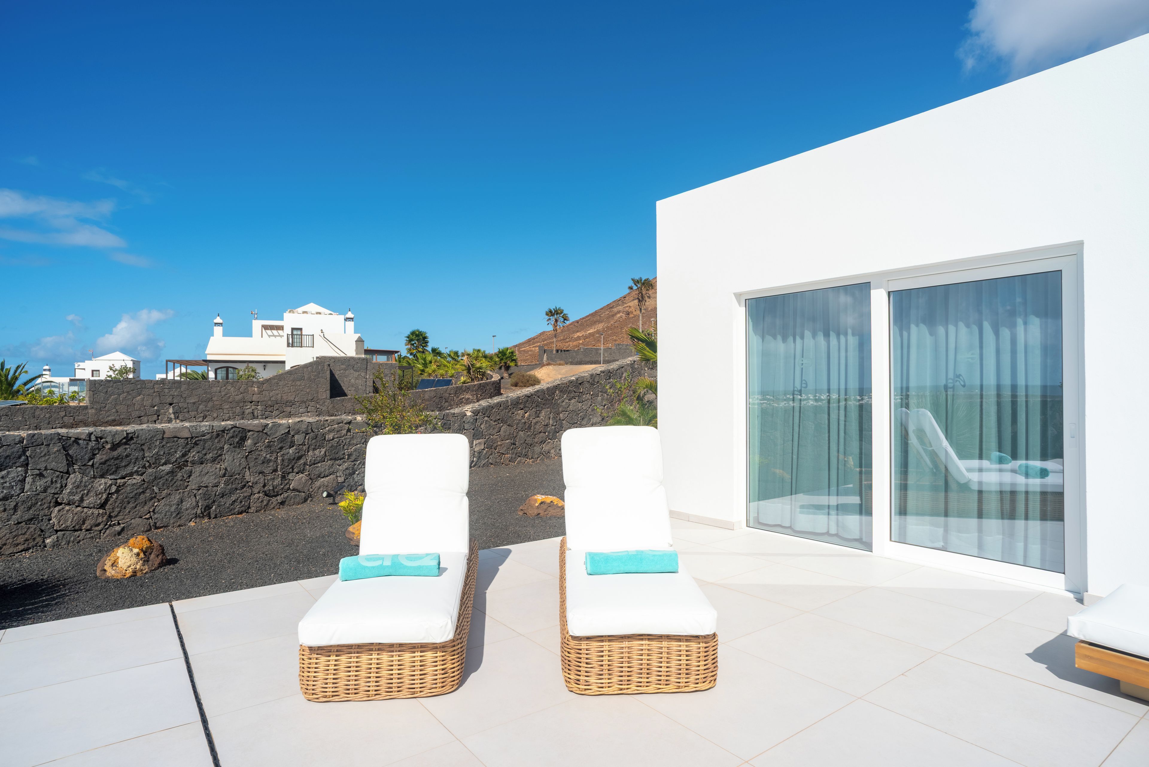 Zona relax esterna moderna con due poltrone in vimini e una porta vetrata che dà sulla piscina.