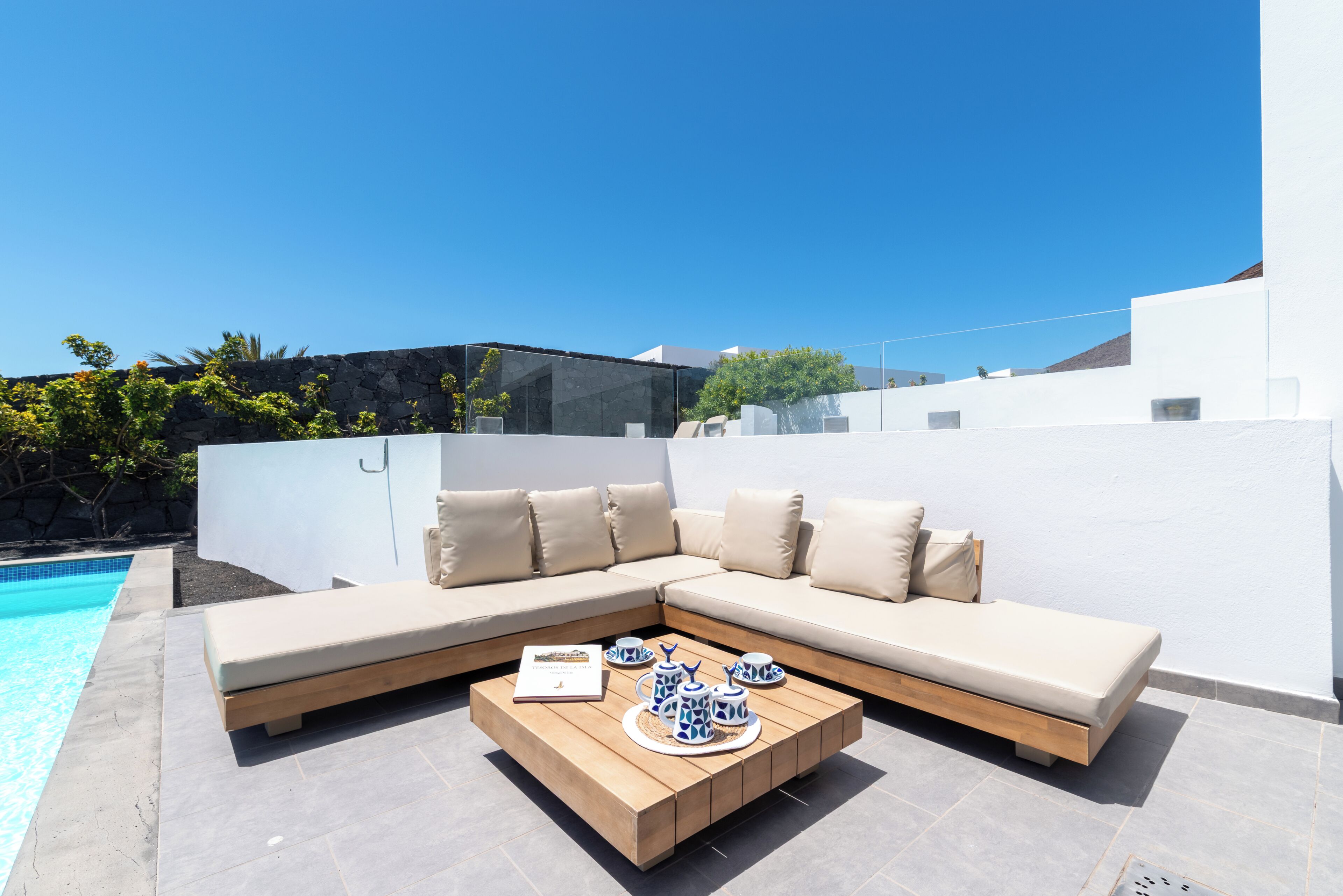 A modern outdoor seating area with a pool, a wooden coffee table, and a beige sectional sofa.