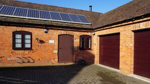 Un edificio de ladrillo con techo solar, un aparcamiento para bicicletas y un letrero que dice 'The Byre'.