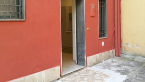 A red building with a door leading to an interior space, a small window with bars, and a light fixture above the door. - Janara - Port' Arsa (Benevento)