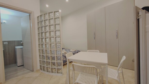 A room with a white table and chairs, a bed with a patterned blanket, a glass partition, and a wardrobe. - Janara - Port' Arsa (Benevento)
