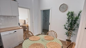 A modern kitchen with a dishwasher, a dining table with woven placemats, wooden chairs, and a potted plant.