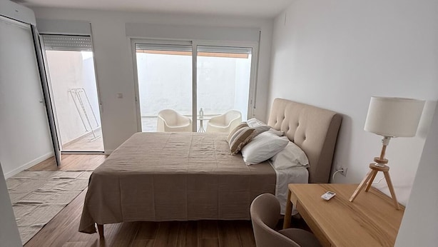 A bedroom with a bed, a desk, and a chair. There is a balcony with chairs and a table.