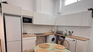 A modern kitchen with white cabinets, a refrigerator, microwave, and a dishwasher. There is a dining table with woven placemats and wooden chairs.