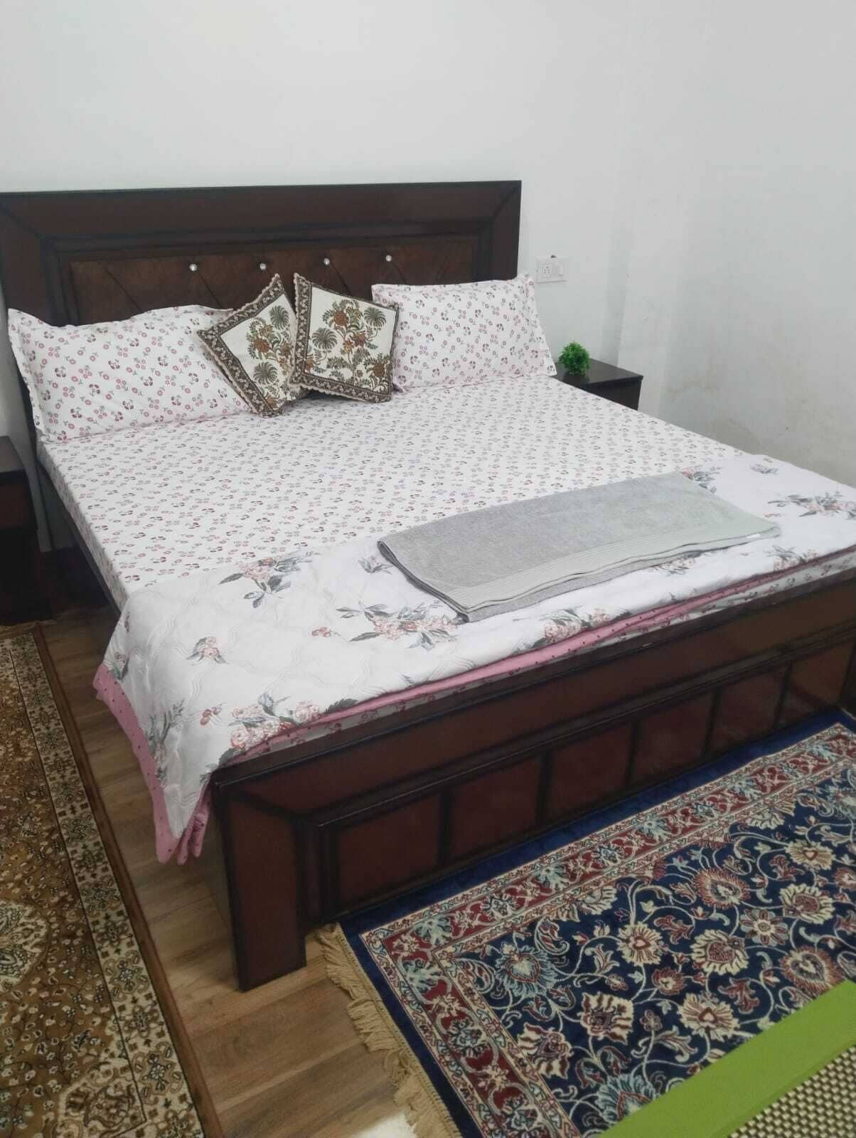 A bed with floral bedding, a headboard, and a nightstand with a lamp.
